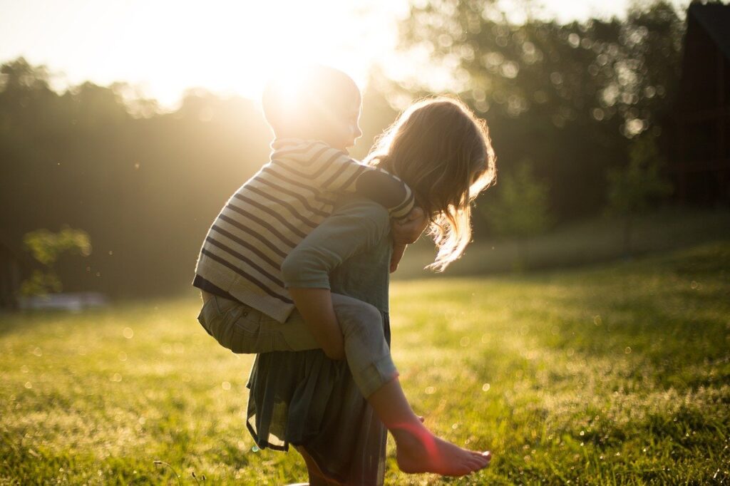 "Au pair cargando en hombros a niño en un día soleado en el parque"